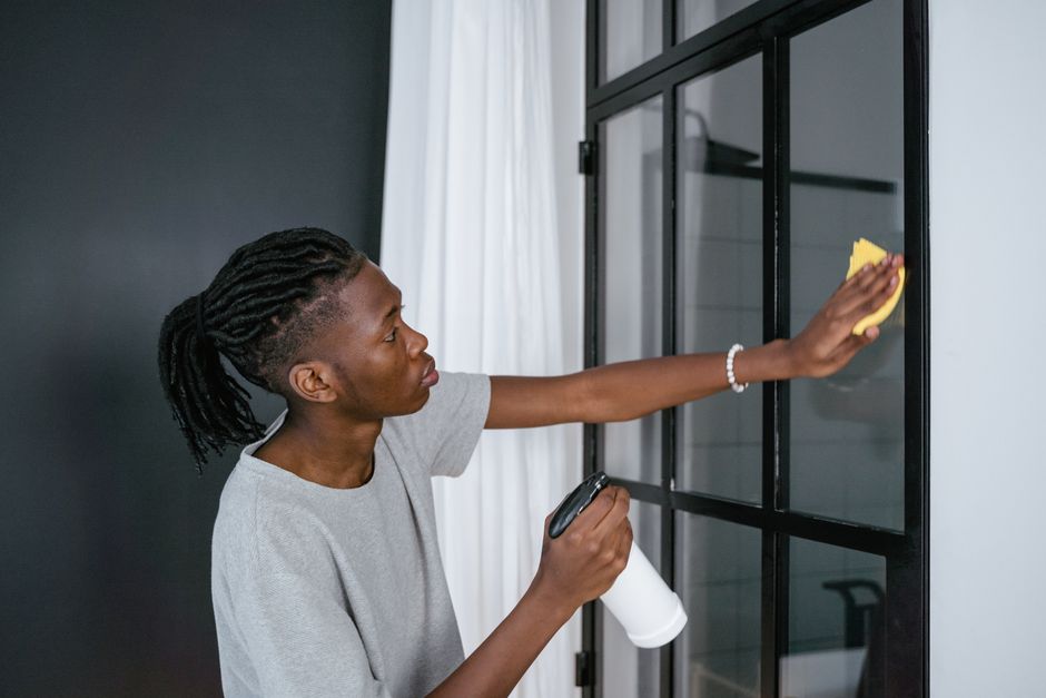 Young man cleaning window indoors using a spray bottle and cloth.