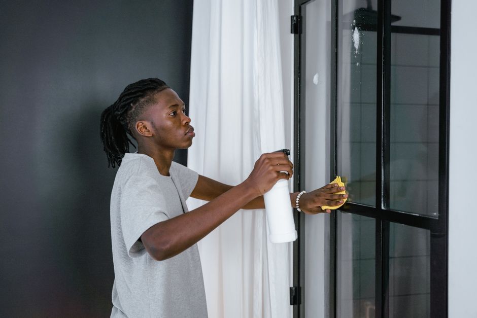 A man cleaning a glass door indoors using a spray bottle and cloth.