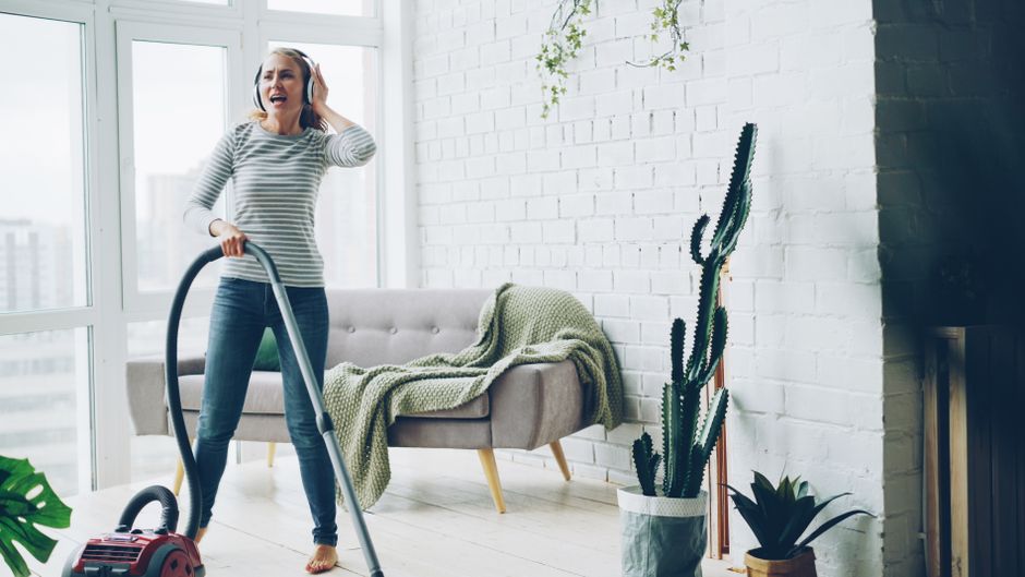 Cheerful woman vacuuming indoors while listening to music.
